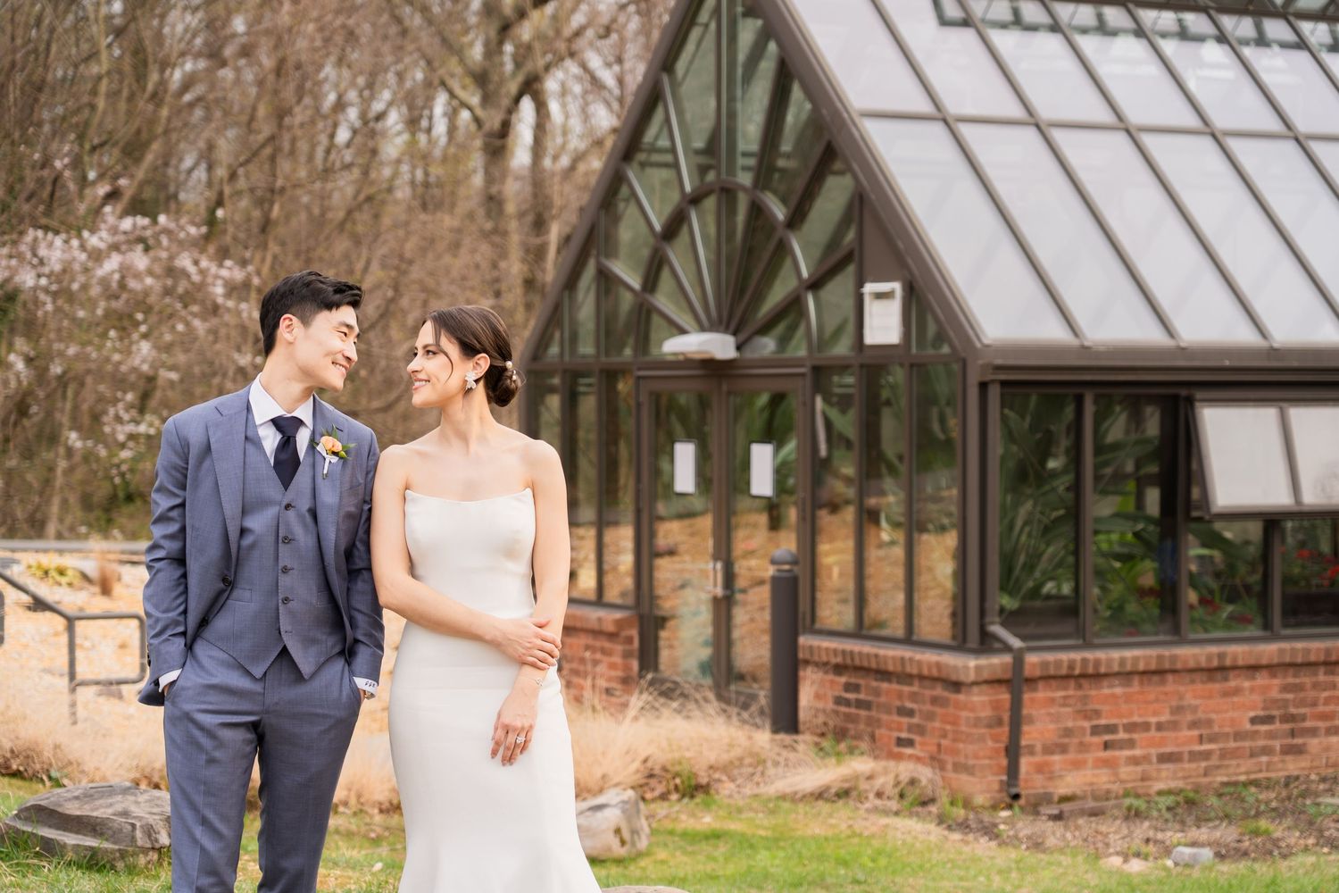 Asian and Romanian couples wedding portrait of a man and woman standing in front of a greenhouse at botanical garden venue.
