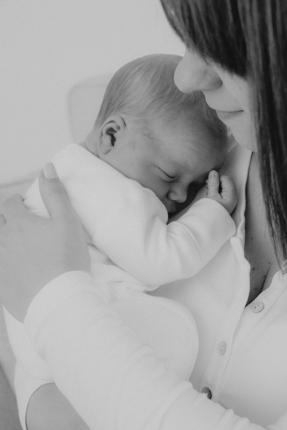 Black and white image of tender moment between parent and sleeping baby in white clothing.