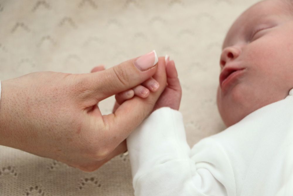 Parent holding newborn baby's tiny hand while infant sleeps peacefully.