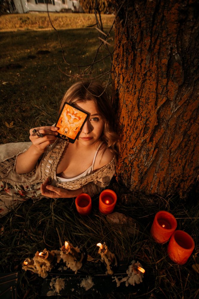 Moody autumn scene with red candles and person holding glowing orange frame by tree.