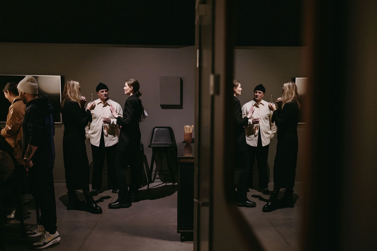 Several people gathered in a dimly lit hallway having informal discussions before or after an event.