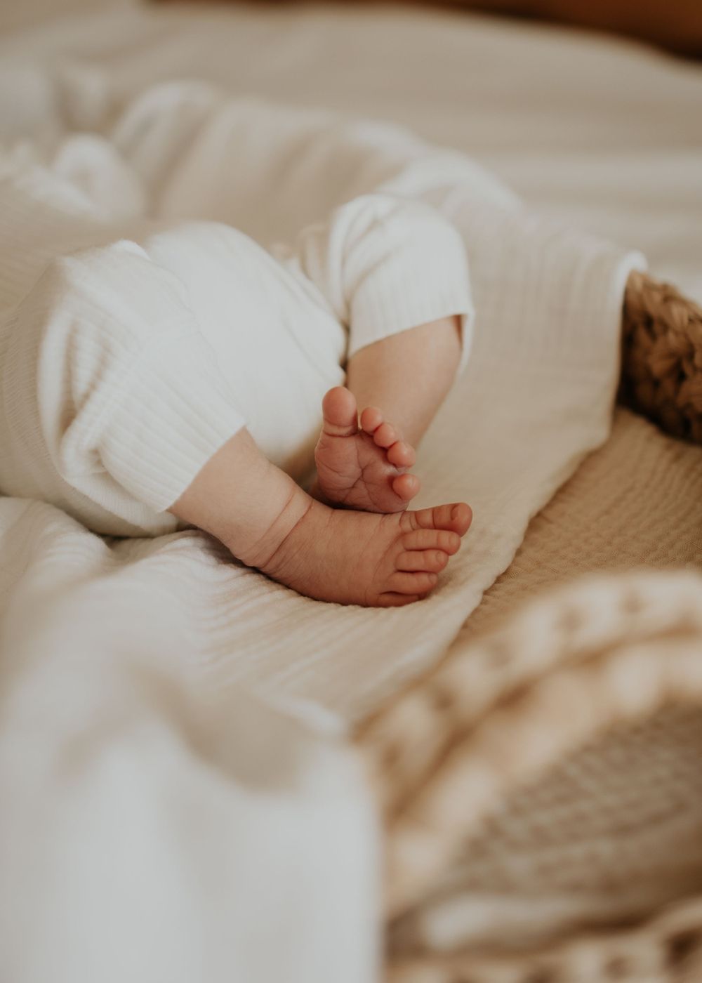 Tiny baby feet peek out from white bedding in a warm, intimate nursery setting.