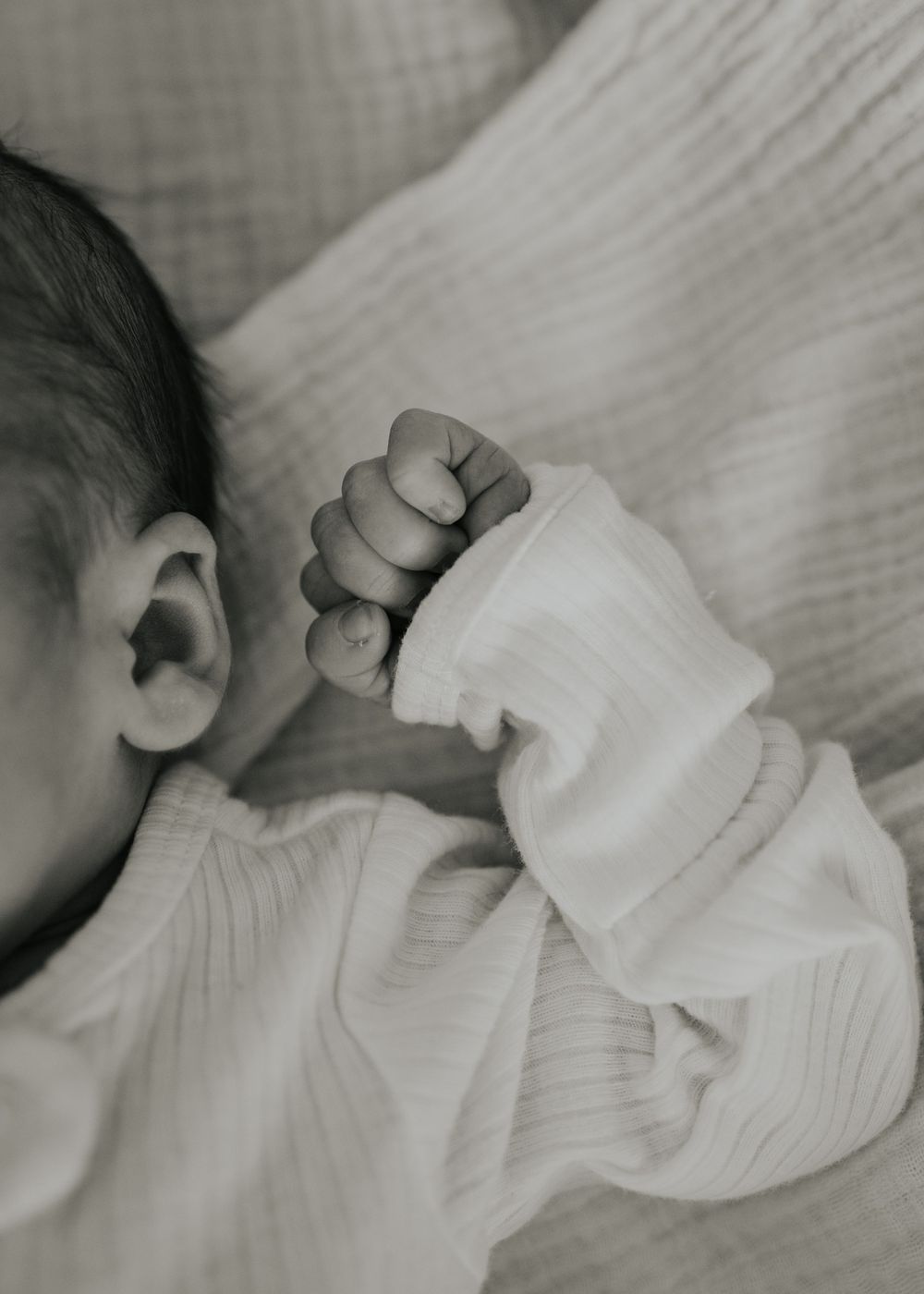 A tiny infant hand grasps soft white fabric while sleeping, captured in black and white.