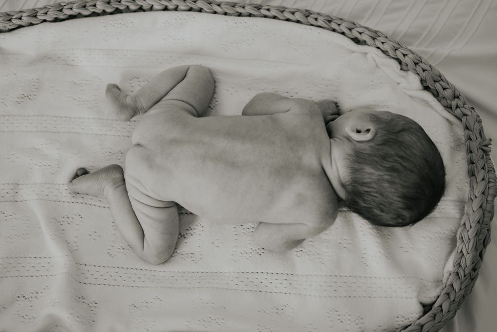 Black and white photograph of a nude newborn baby lying on their stomach on white textured fabric.