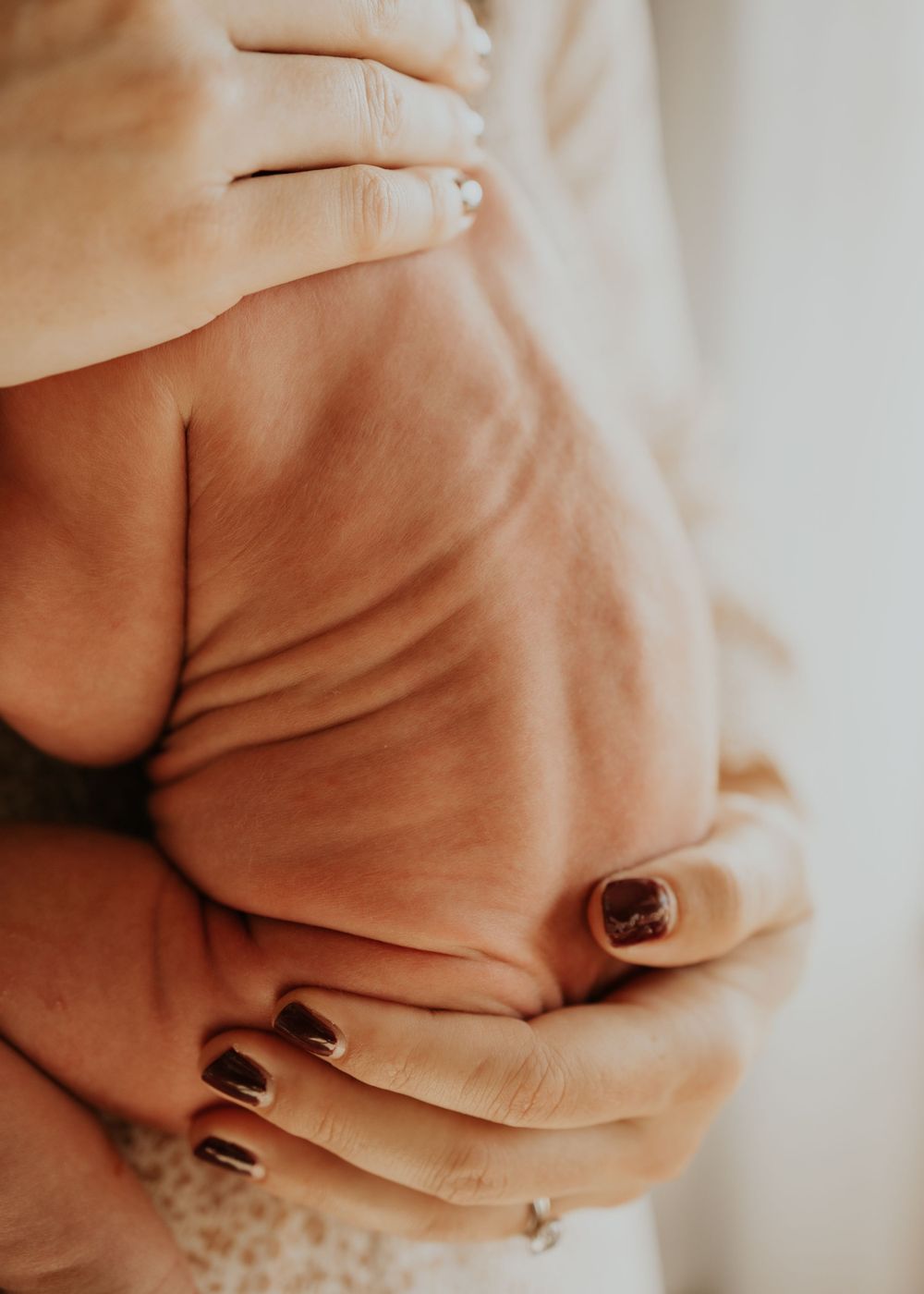 Close-up view of dark painted fingernails on hands with soft beige fabric in warm lighting.
