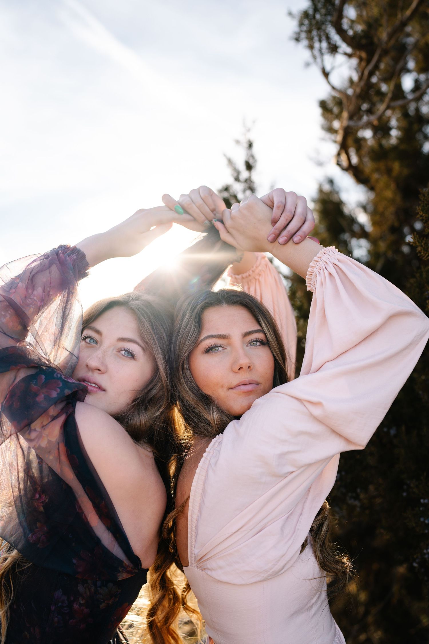 Two friends in elegant dresses pose artistically in backlit golden sunshine.