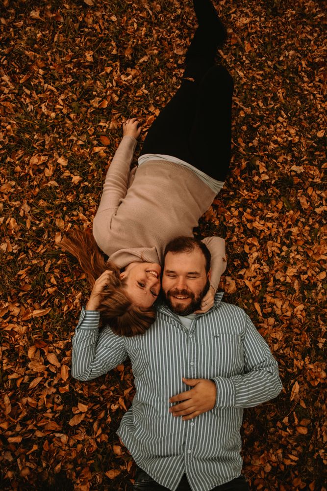 Couple lying together on colorful autumn leaves during romantic photoshoot.