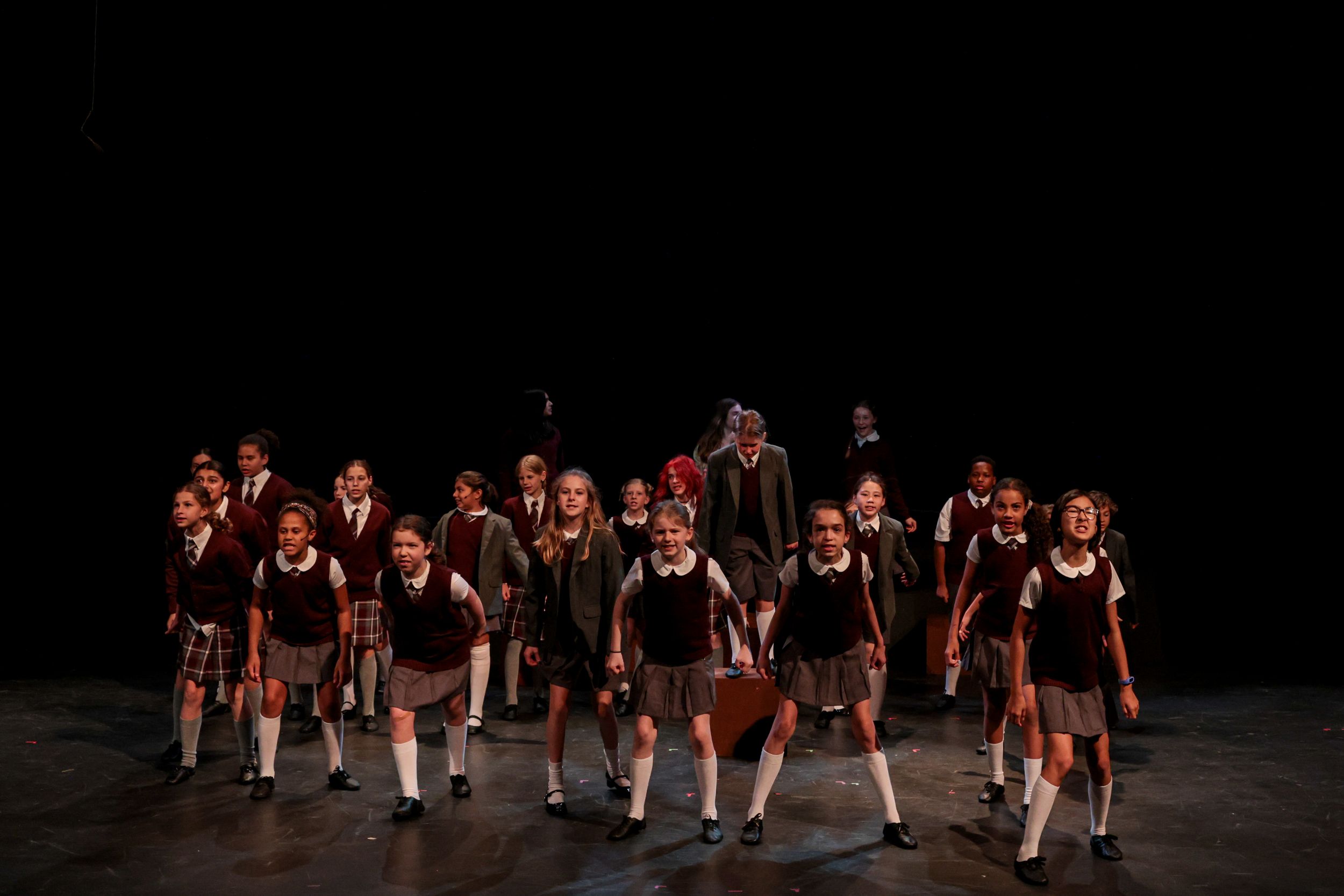 Group of performers in dark uniforms stand together on a dark stage during a theatrical production. Theatre photography.