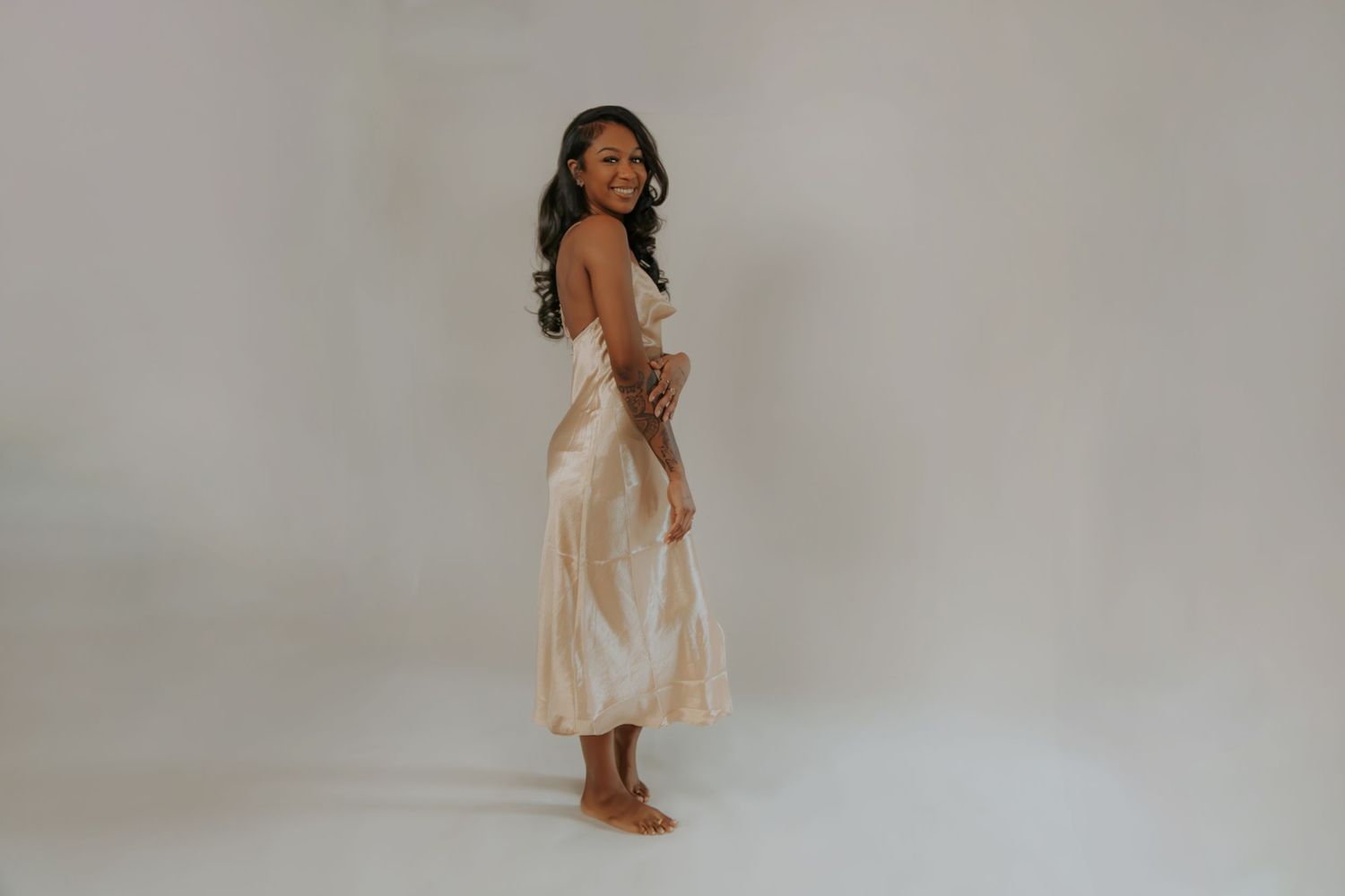Subject in cream slip dress creates artistic poses during intimate portrait session.