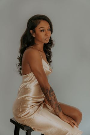 Subject in cream silk slip dress poses artistically from side angle on minimal grey set.