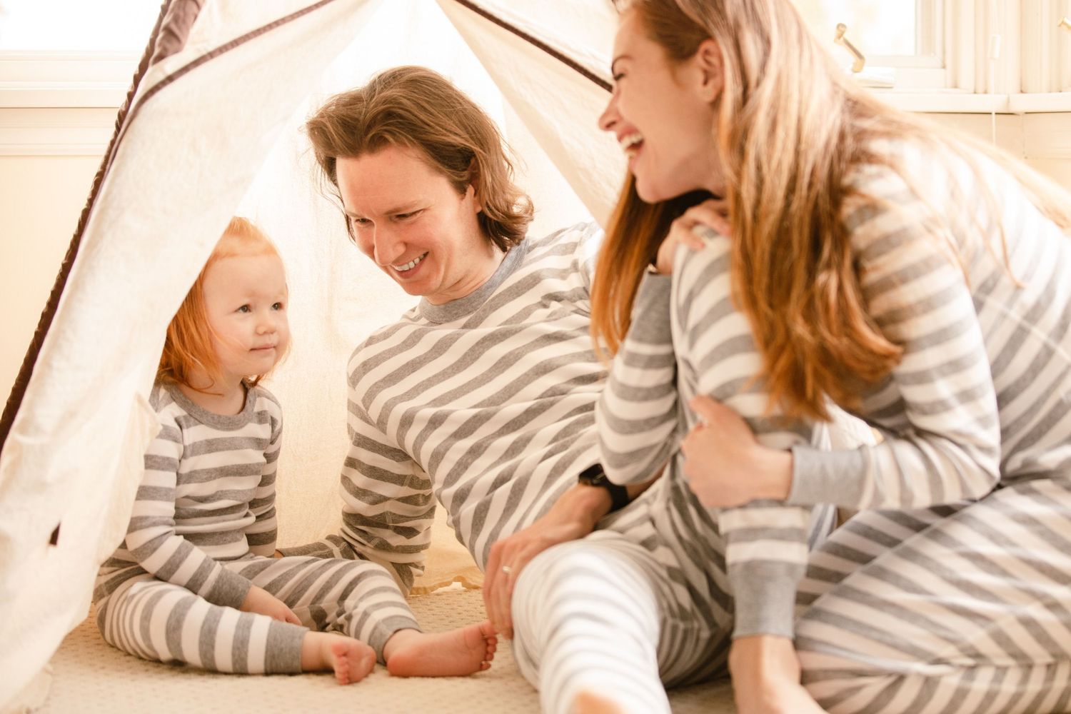 A family wearing matching gray and white striped sweaters sits together, smiling and enjoying quality time at home.