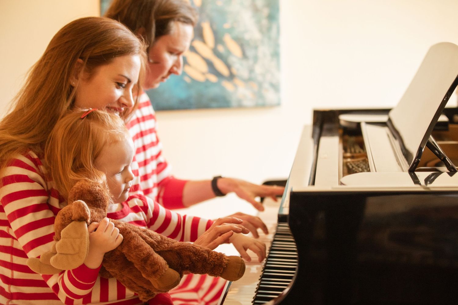 A piano lesson at home shows people wearing matching red and white striped shirts playing together.
