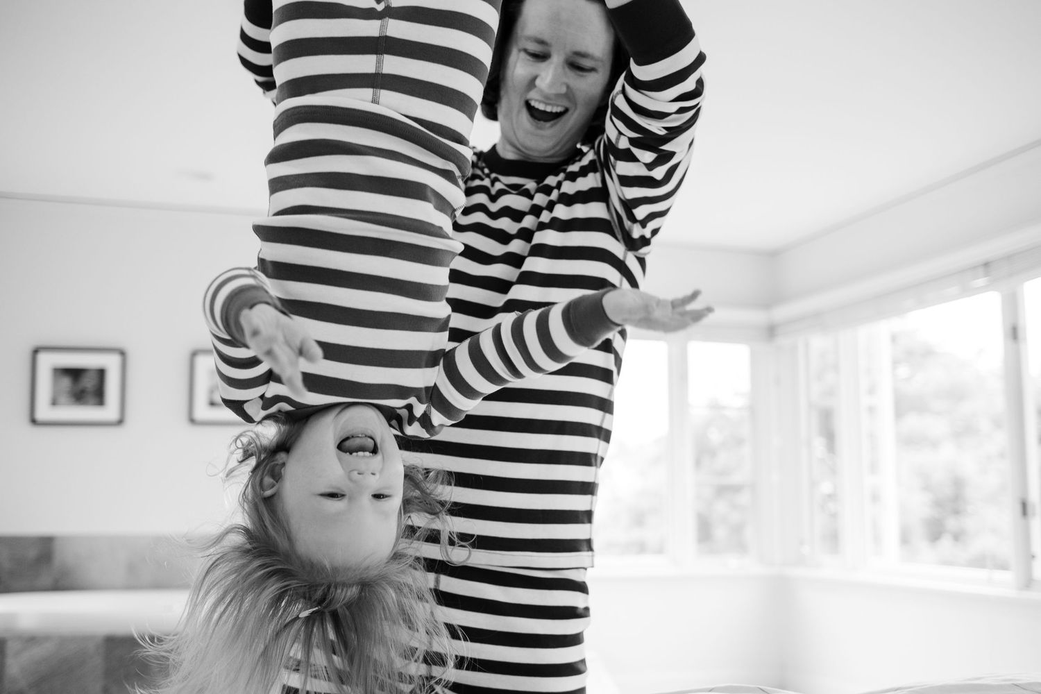 A playful black and white image showing someone in a striped shirt holding a happy child upside down.