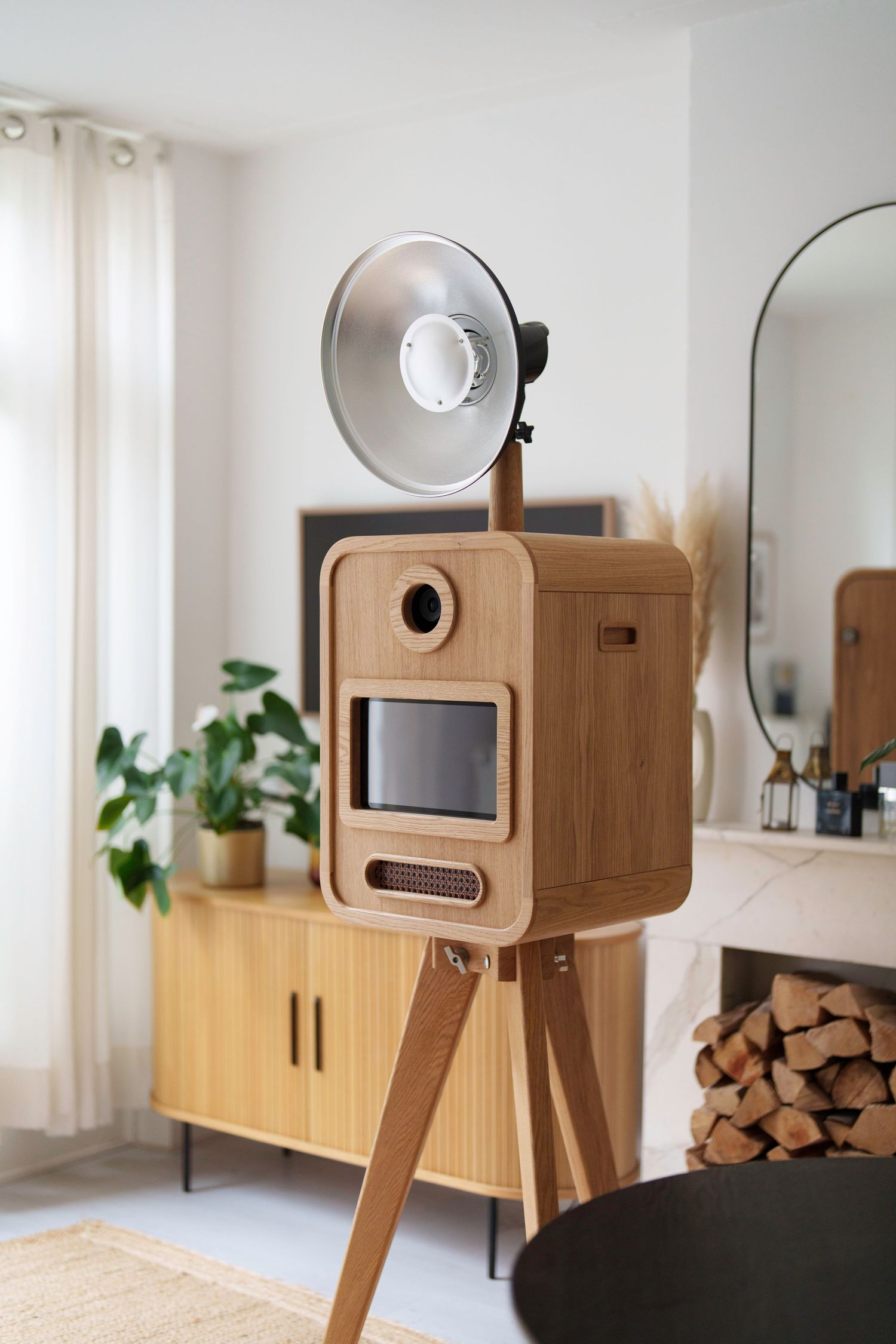Elegant oak wood photo booth with studio flash on tripod stands in a bright modern Scandinavian interior.