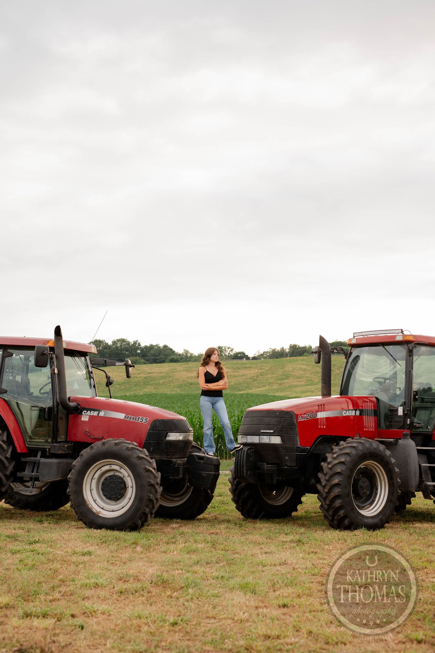 Person poses victoriously atop red tractors in countryside setting.