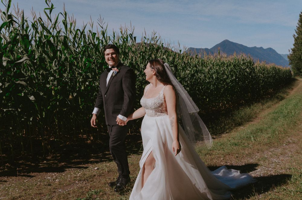 A couple walks along a path beside a cornfield with scenic mountain views on their wedding day.