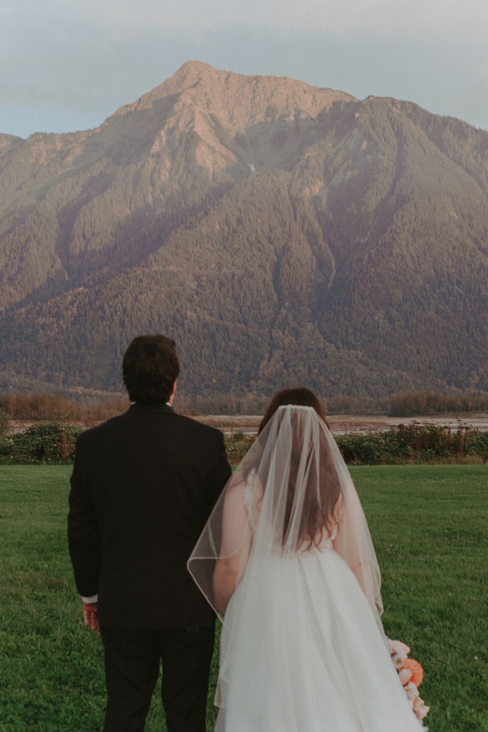 A couple in wedding attire stands looking at a majestic mountain range on their special day.
