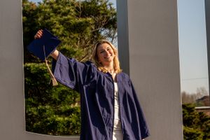 Girl holding graduation cap and wearing a graduation gown, smiling proudly.