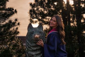 Girl in graduation gown touching the nose of UConn's iconic Jonathan the Husky statue for a celebratory graduation tradition.