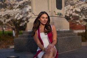 Woman in a white dress sitting amidst cherry blossoms, smiling proudly for her graduation photo.