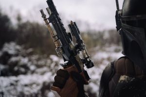 Mandalorian cosplay with gun in focus and half of the helmet visible on the right side, highlighting detailed armor and weaponry.