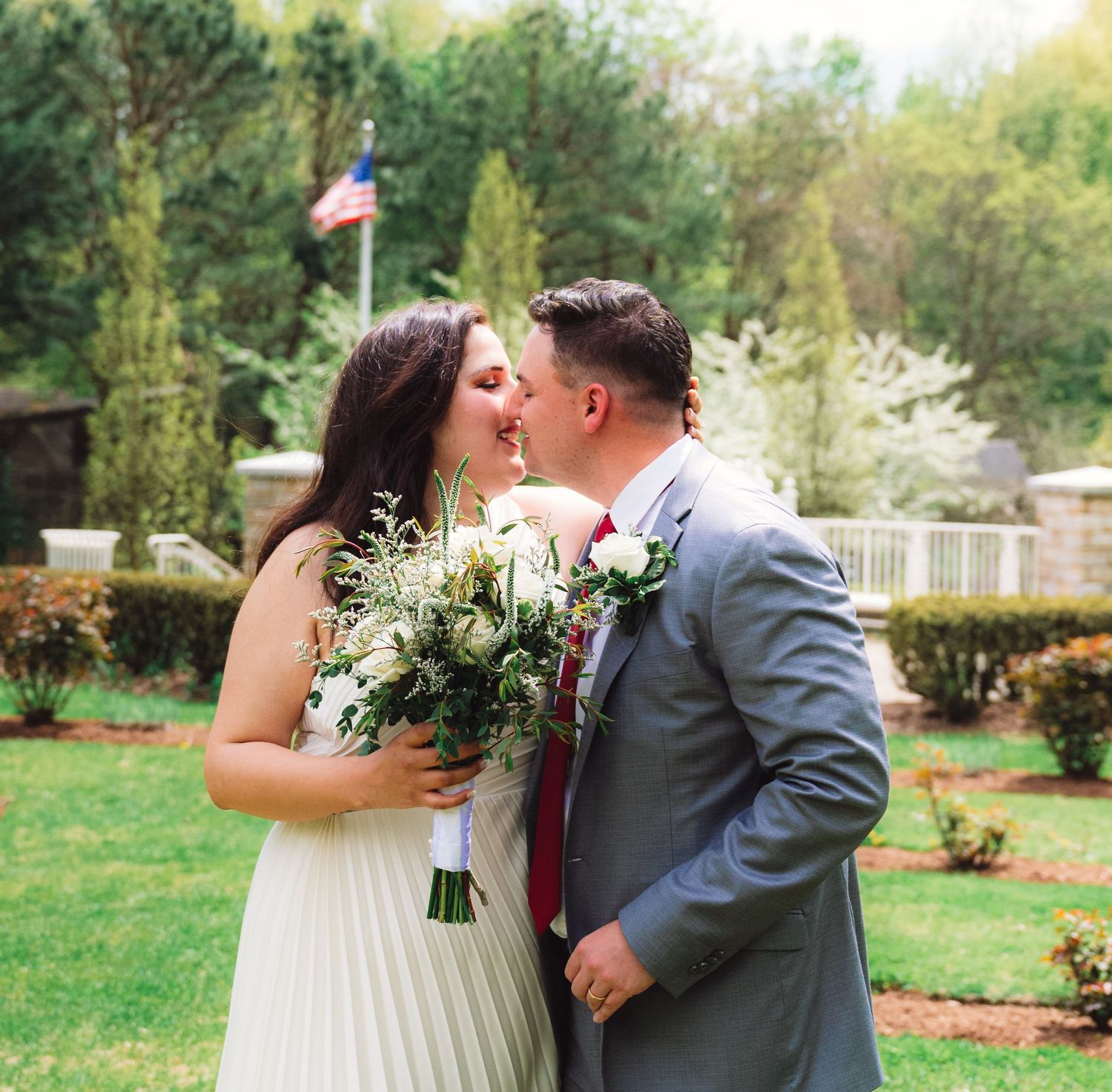 A couple sharing a romantic moment in a garden with a bouquet of white flowers.