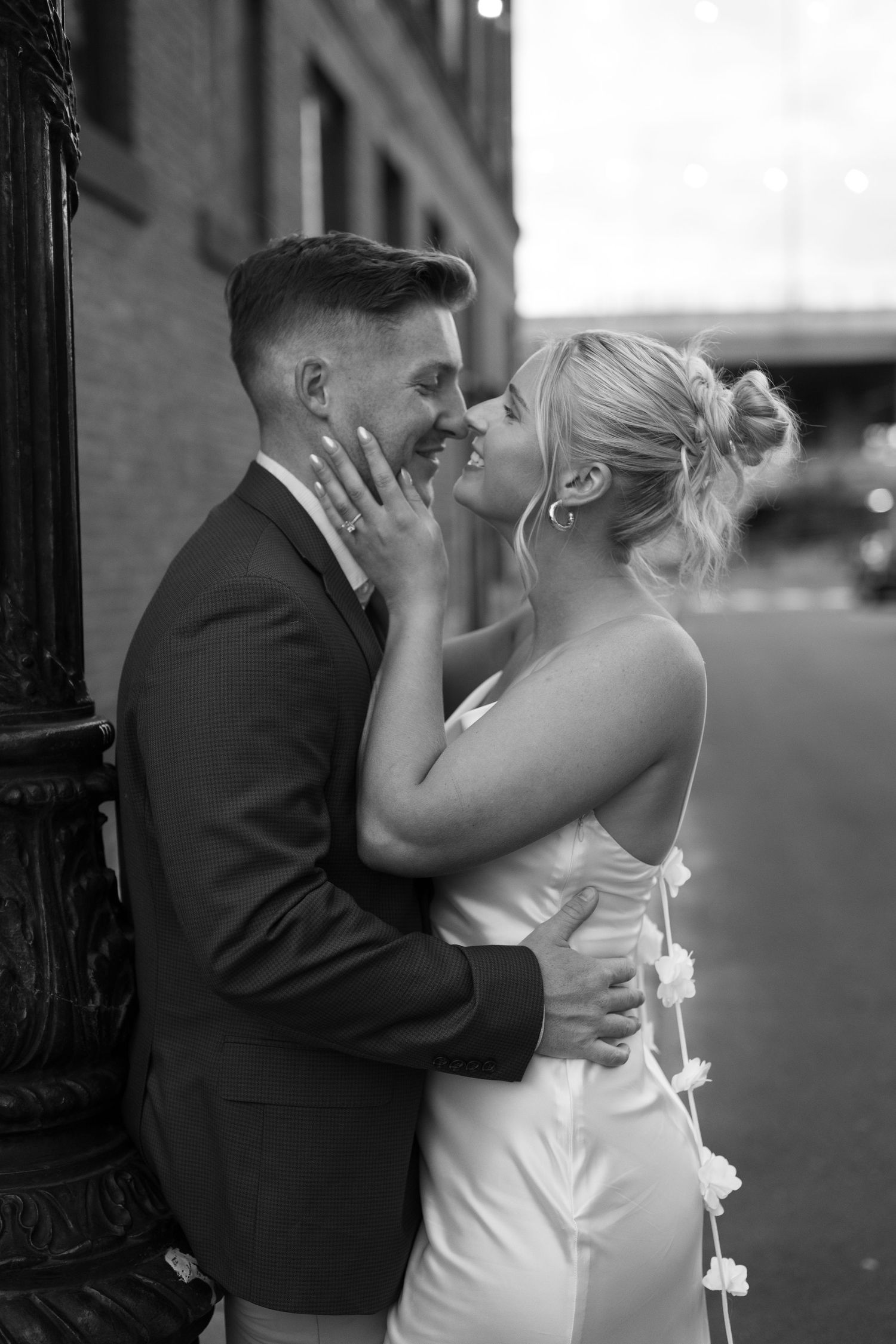 A black and white wedding photo of a couple sharing an intimate embrace against an urban backdrop.