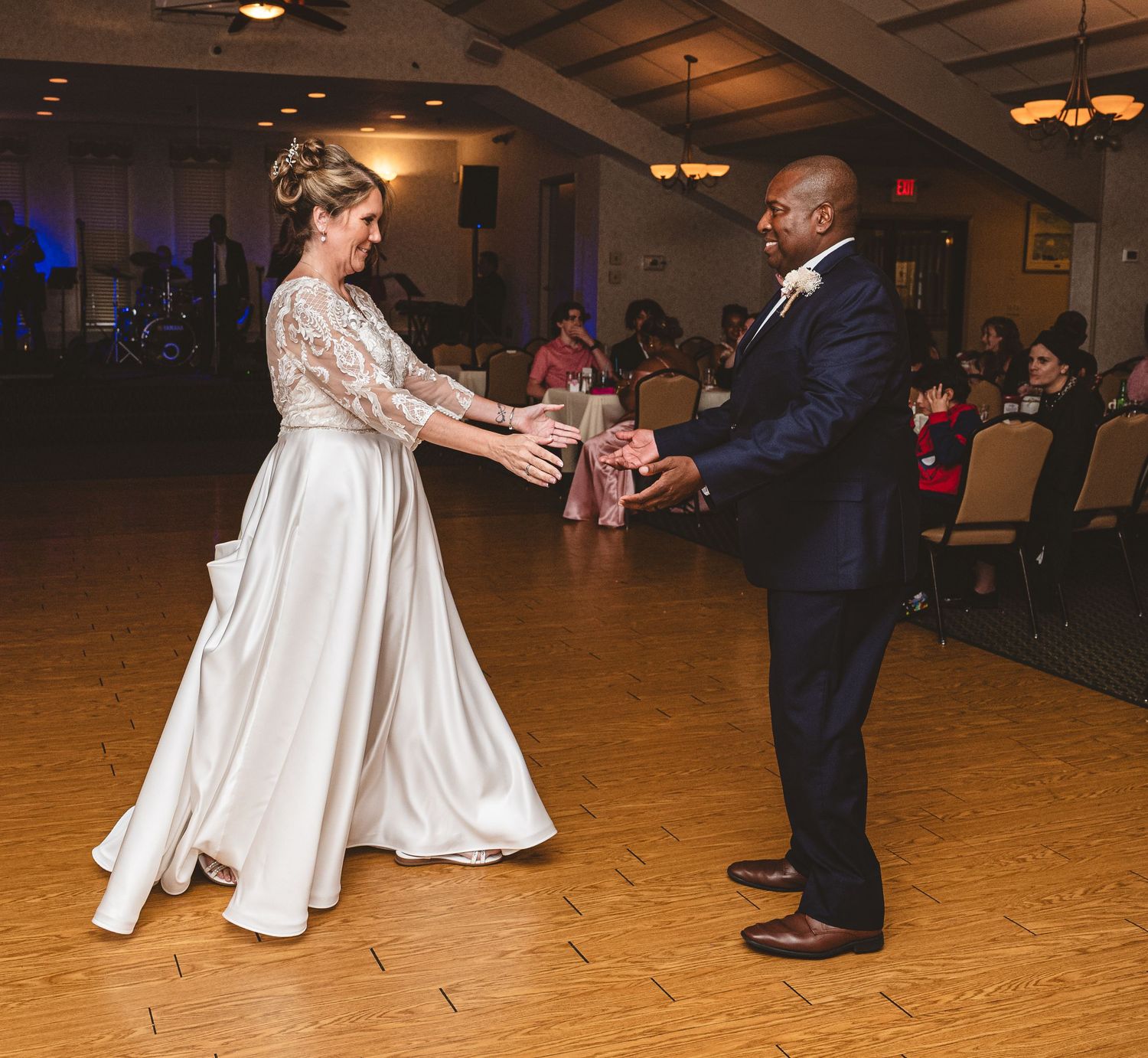 A couple dances together on a wooden floor during their wedding reception in an indoor venue.