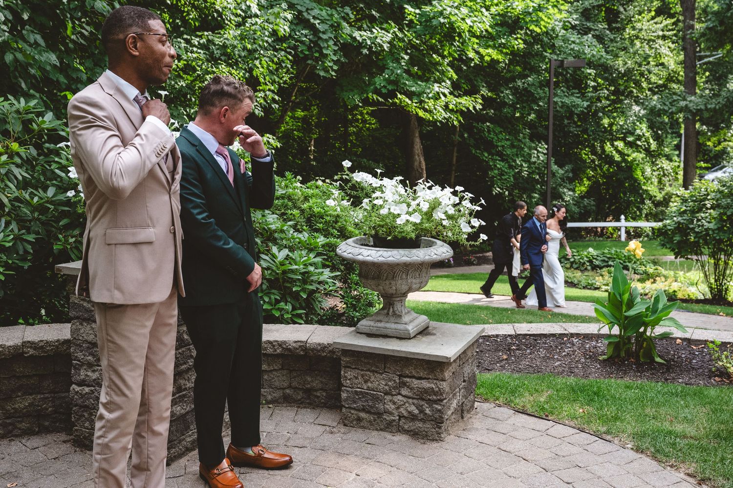 A couple in formal attire shares a romantic moment in a lush garden setting during a special occasion.