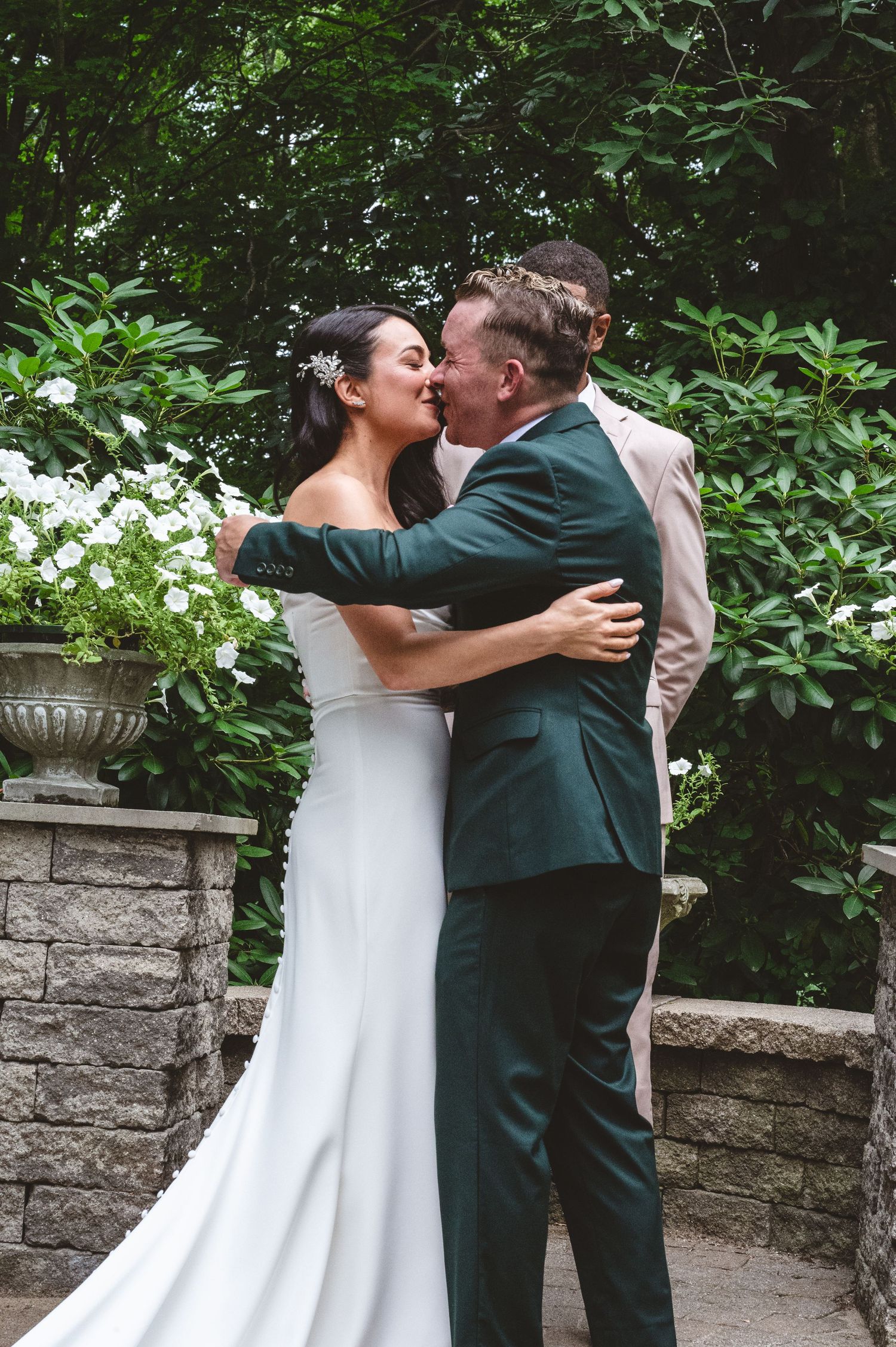 A couple embracing during their wedding ceremony in a lush garden with stone architecture.