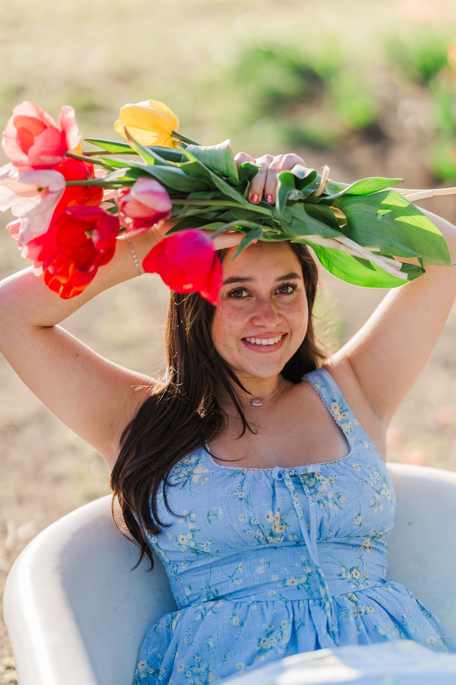 Colorful tulips arc overhead as someone in a light blue floral dress relaxes in an outdoor chair.