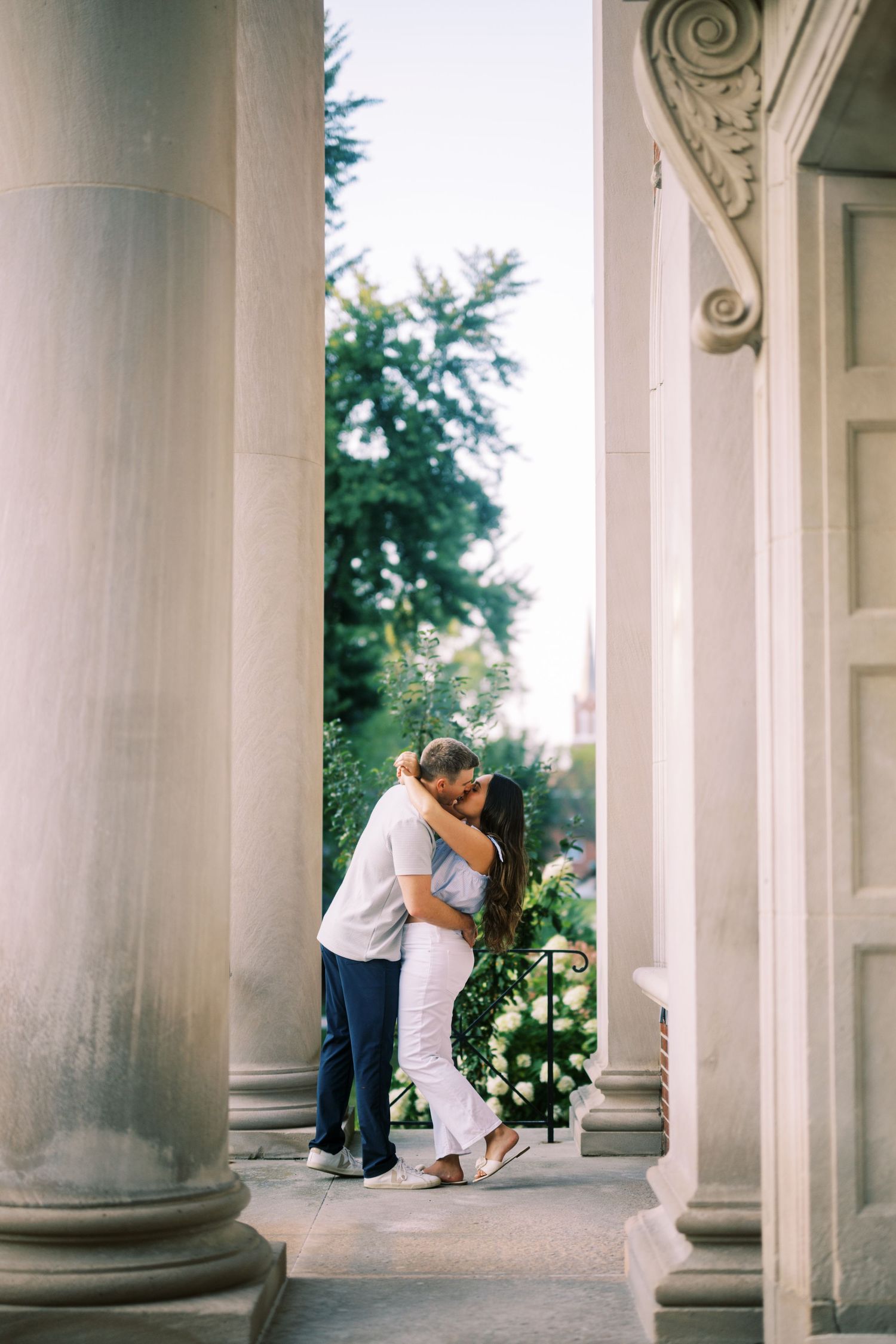 A romantic moment captured between two people embracing between classical white columns on a porch.