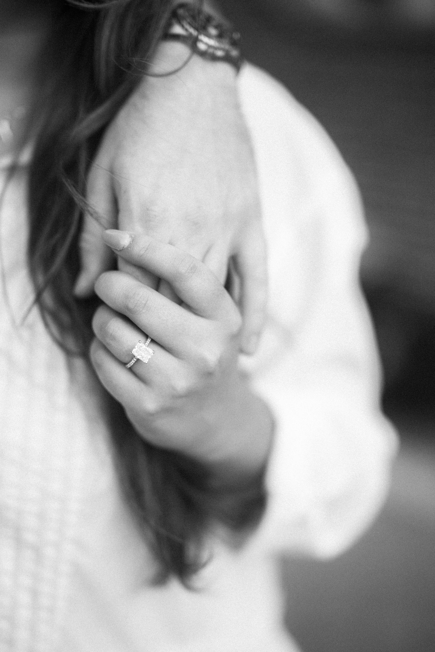 An elegant black and white close-up shot of hands showing a simple ring on woman's finger with soft focus background.