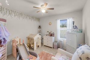 Modern nursery room with white furniture, wooden house bed frame, and neutral decor in a bright space.