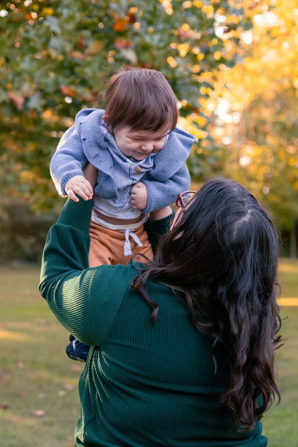 Mom holds her toddler up in the sunset light while facing away from the camera.