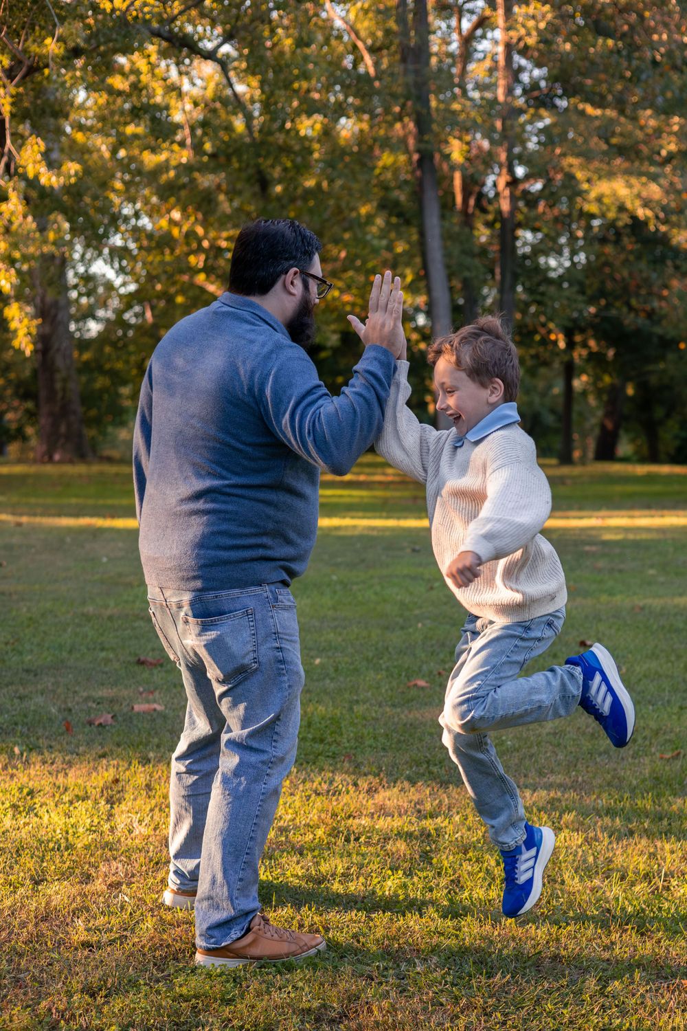 Dad holds his hand up for a young boy who has run and jumped to give a high five.