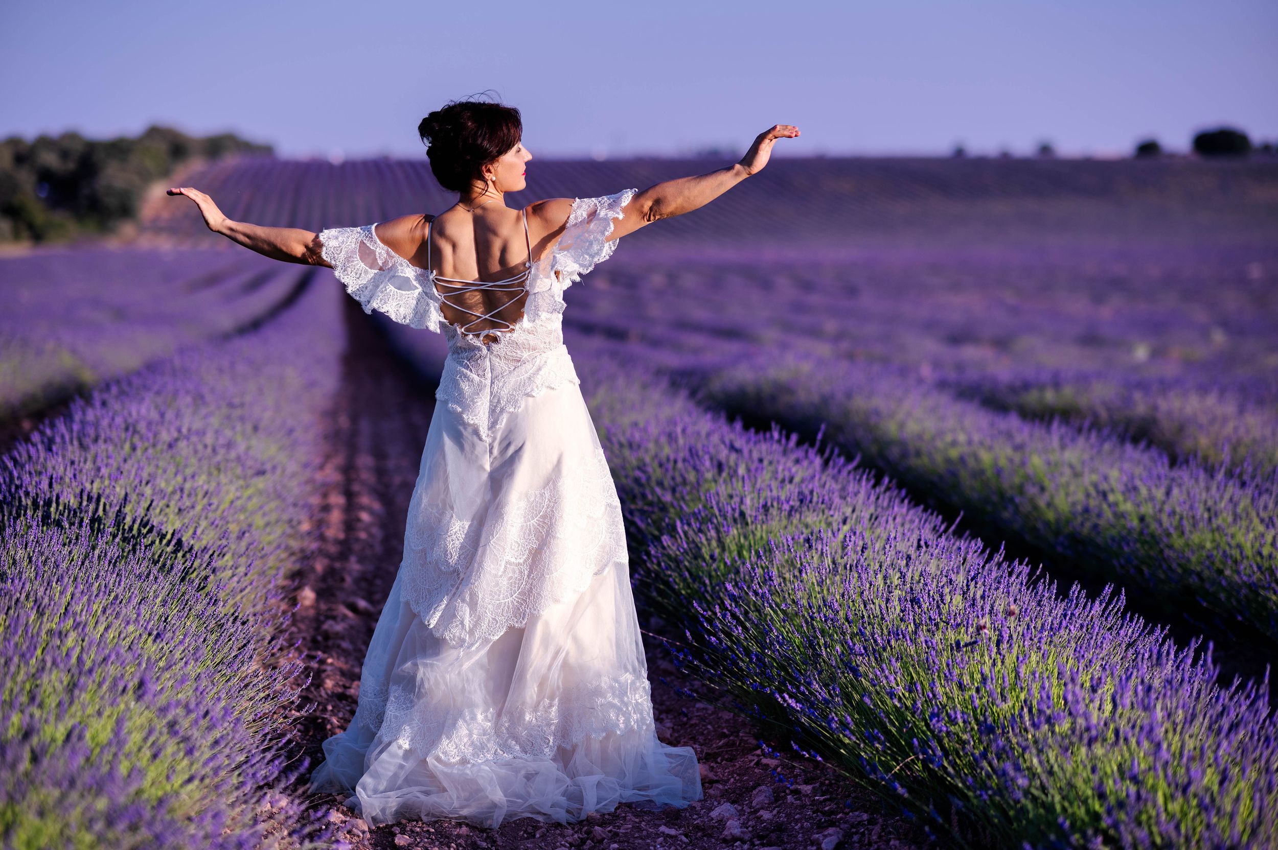 A white lace dress flows gracefully in a blooming purple lavender field during sunset.