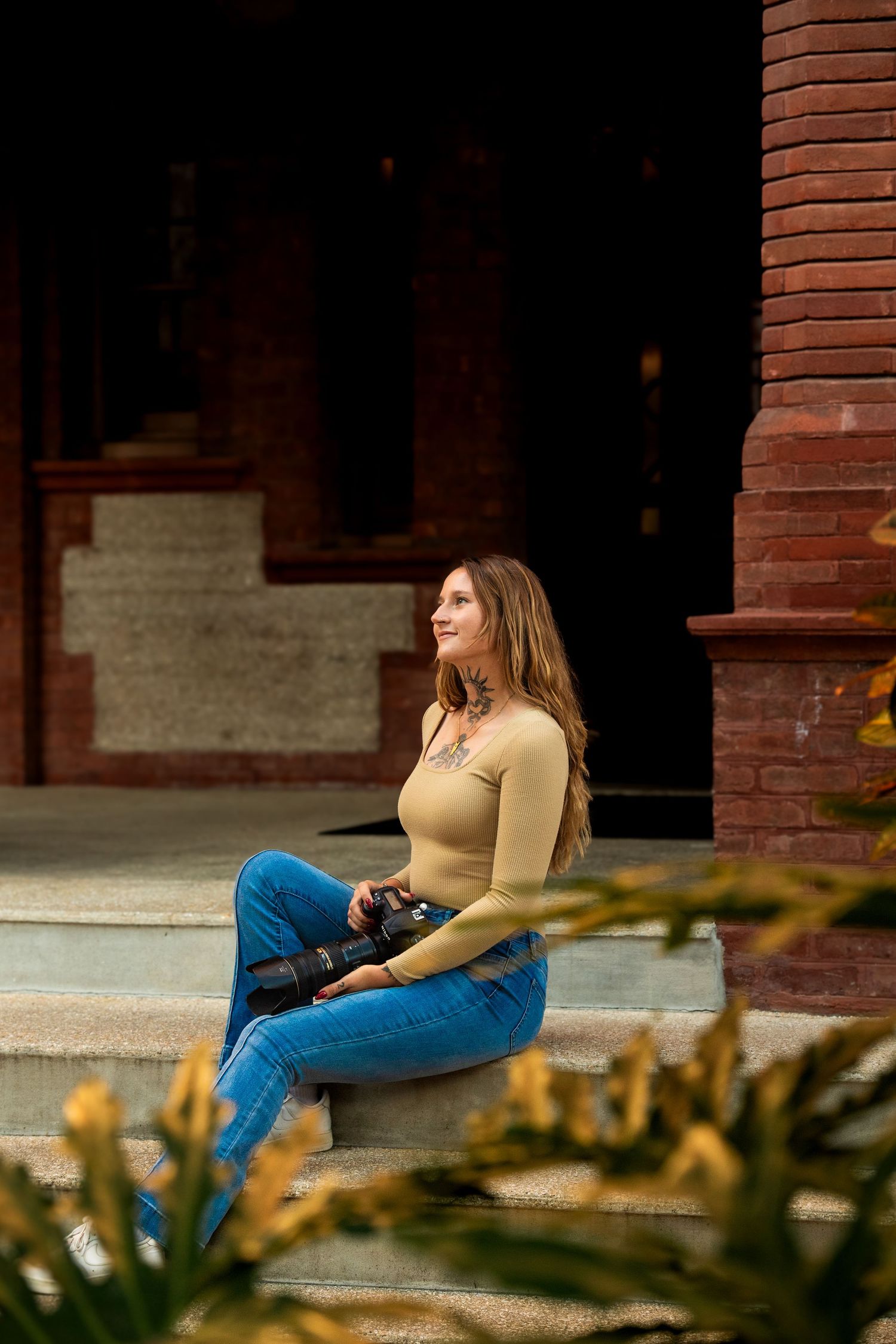 Someone relaxing on stone steps with red brick architecture and greenery in the background.