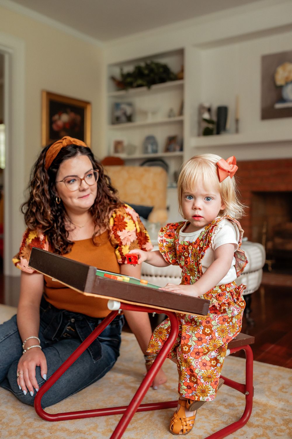 Pair in coordinating orange outfits sit together at a red metal table while looking at a book in cozy living room.