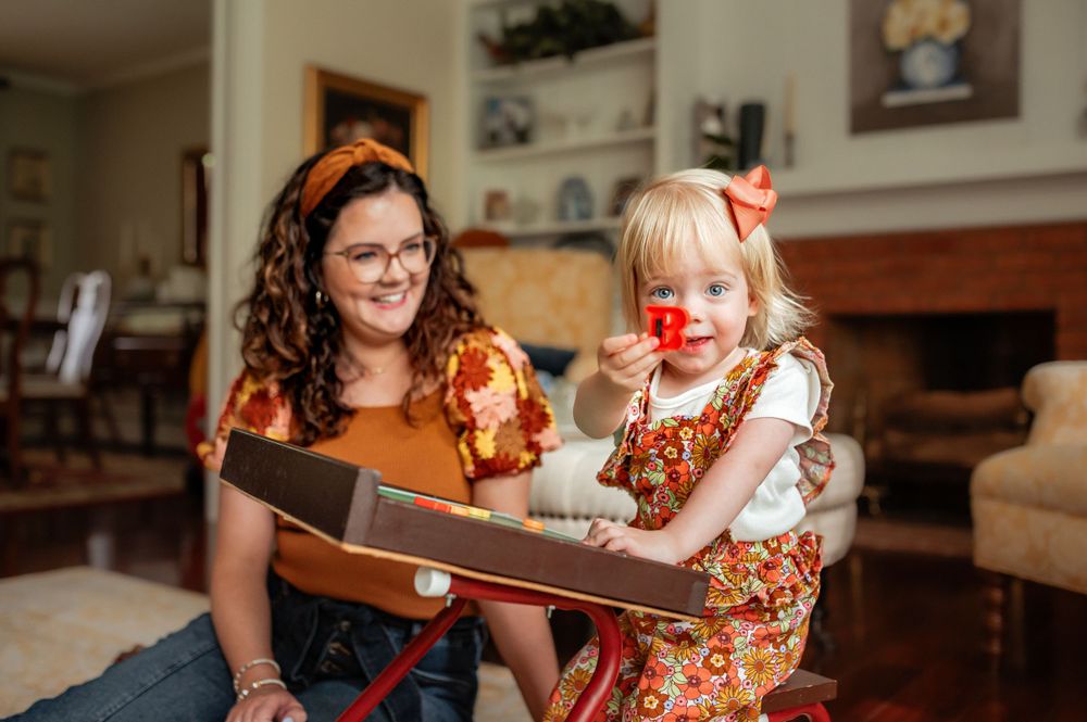 Two people reading a storybook together in a cozy living room while wearing autumn-colored floral outfits.