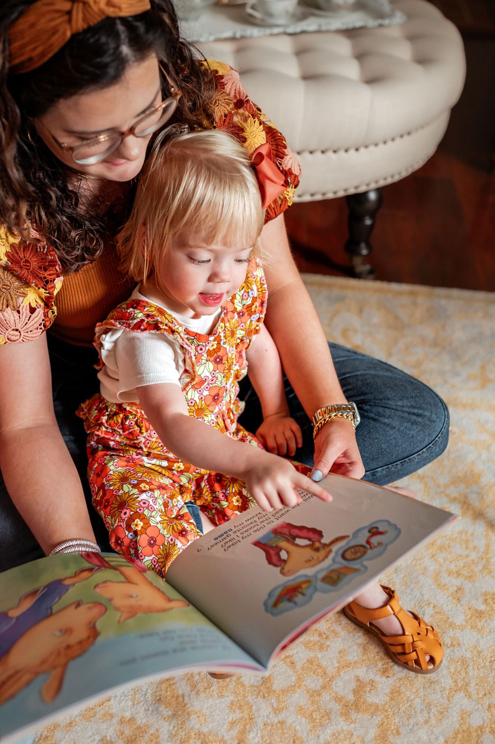 A warm moment of reading together on a patterned rug while wearing matching floral outfits.