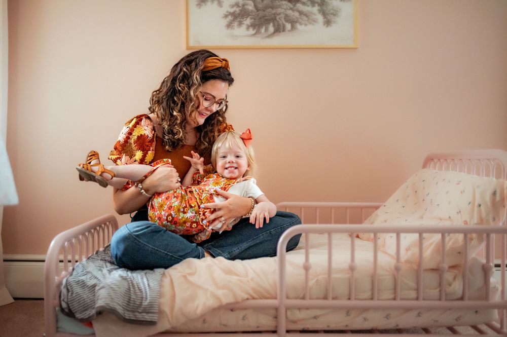 A tender moment of connection while sitting together on a bed in a nursery with pink walls.