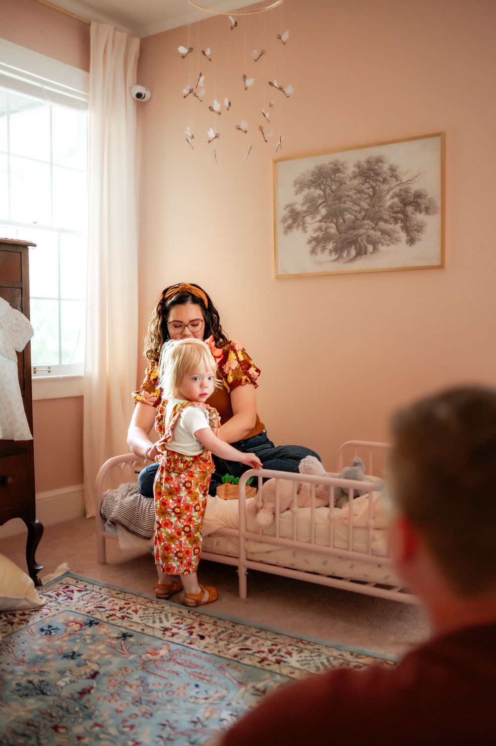 A cozy children's bedroom with pink walls, butterfly decorations, and a vintage style metal bed frame on a patterned area rug.