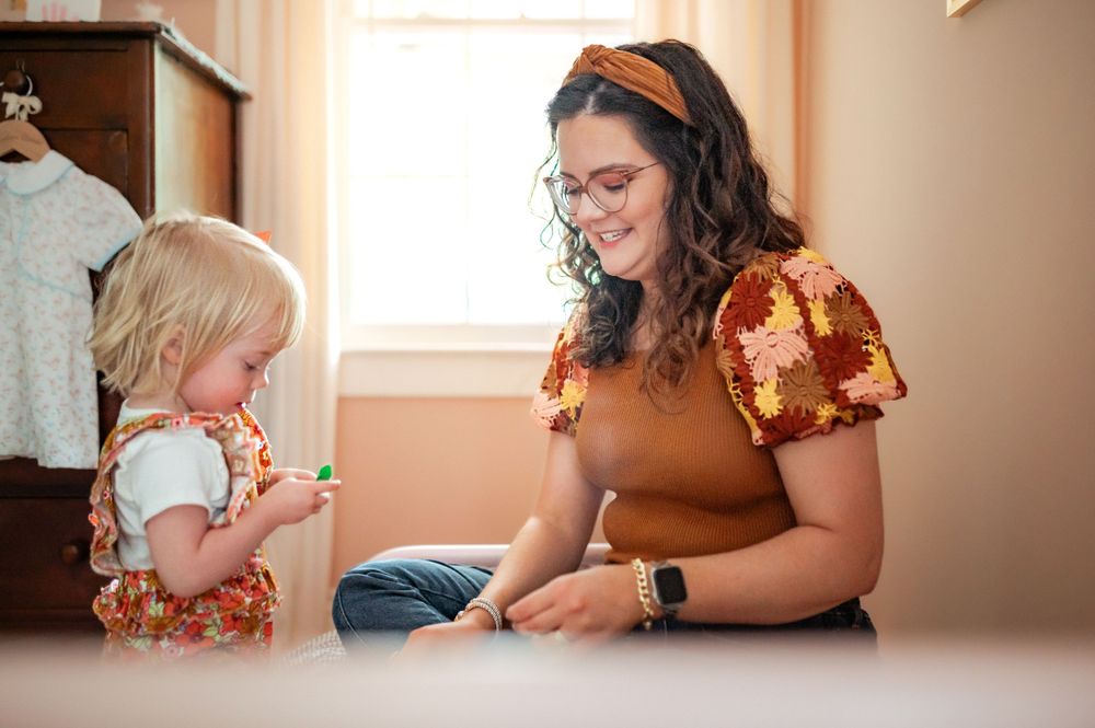 A parent and small child sit on the floor together, wearing matching floral print clothing in warm autumn colors.