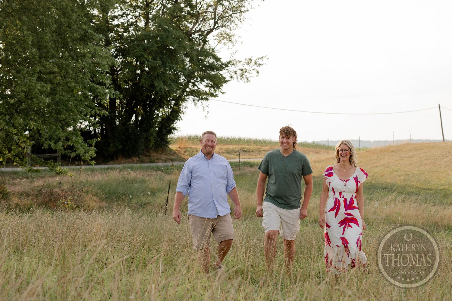 Three people walk together through a grassy field on a summer evening.