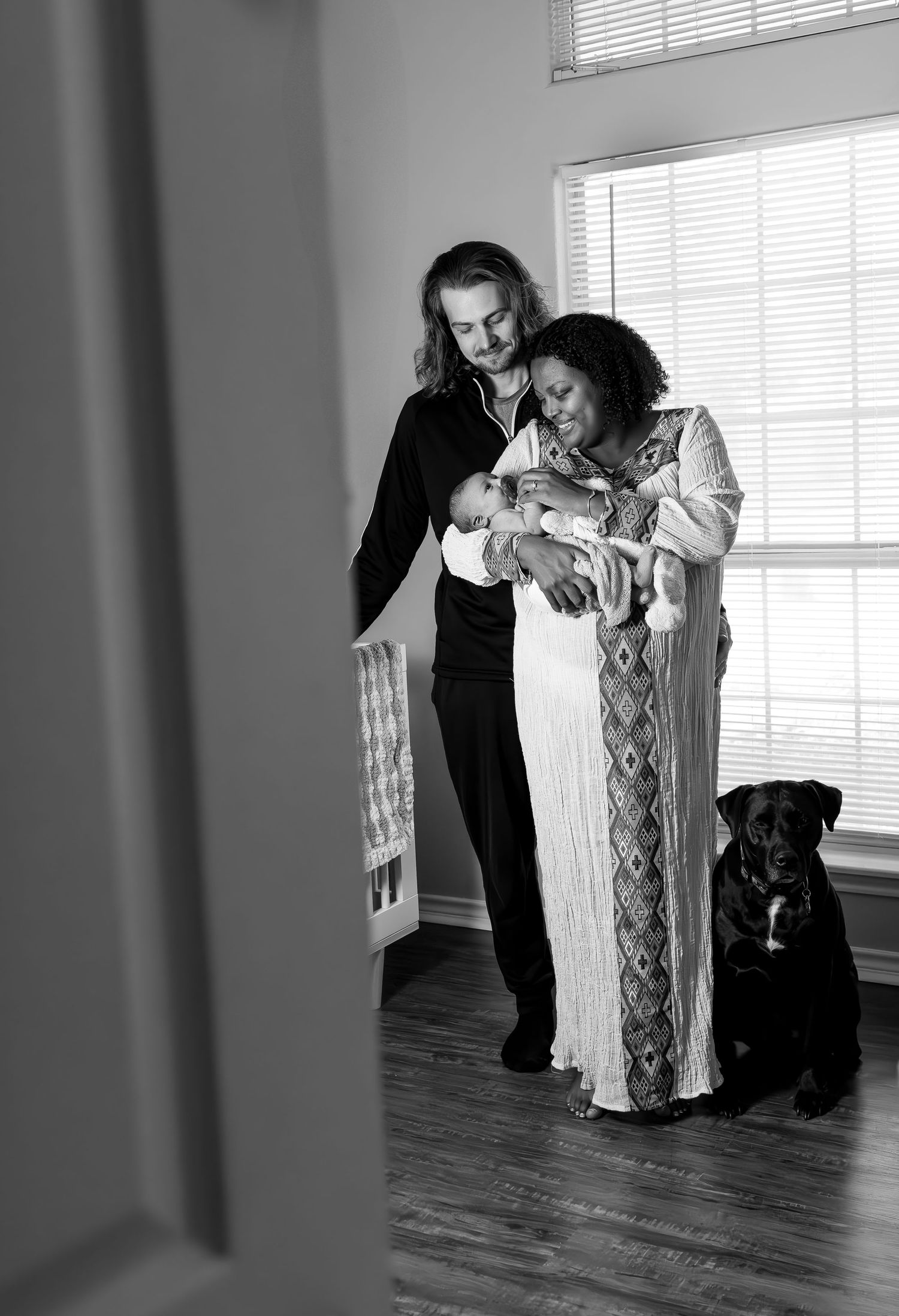 In home newborn session of baby with family dog sitting on floor next to them.