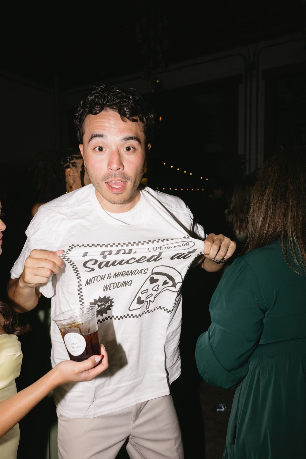 Man proudly displaying a white wedding t-shirt reading 'Sauced Up' at Mitch and Miranda's wedding reception.
