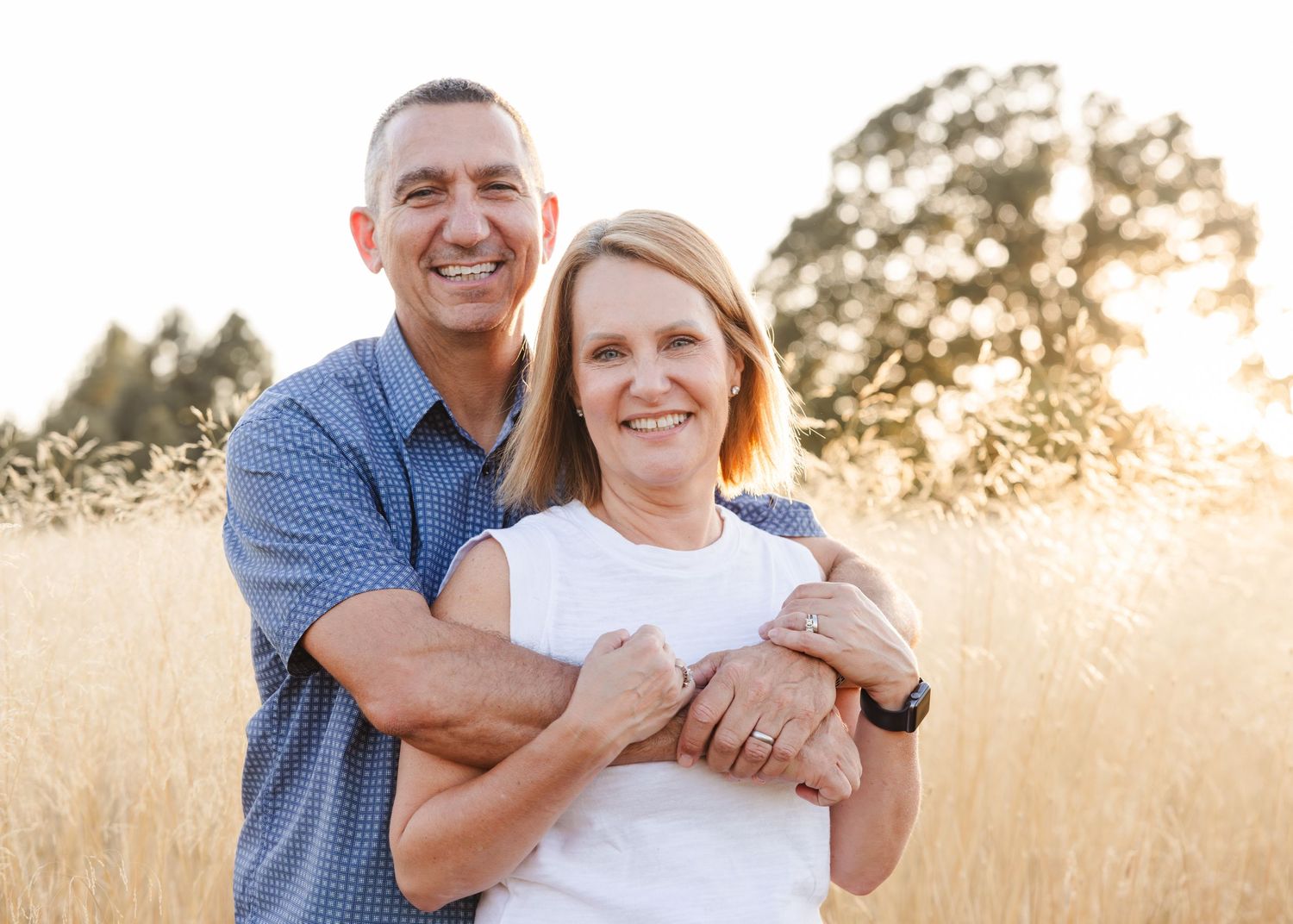 A couple embraces in a sunlit meadow of golden grass during sunset, creating a warm and romantic outdoor portrait.