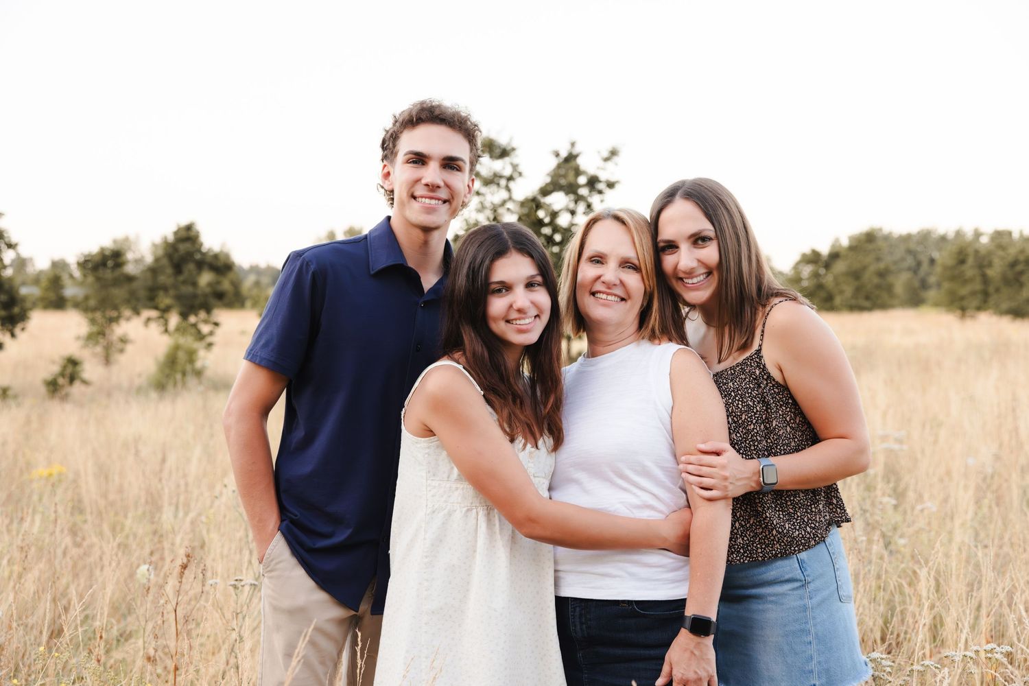 A group stands together smiling in a golden field of tall grass during sunset.