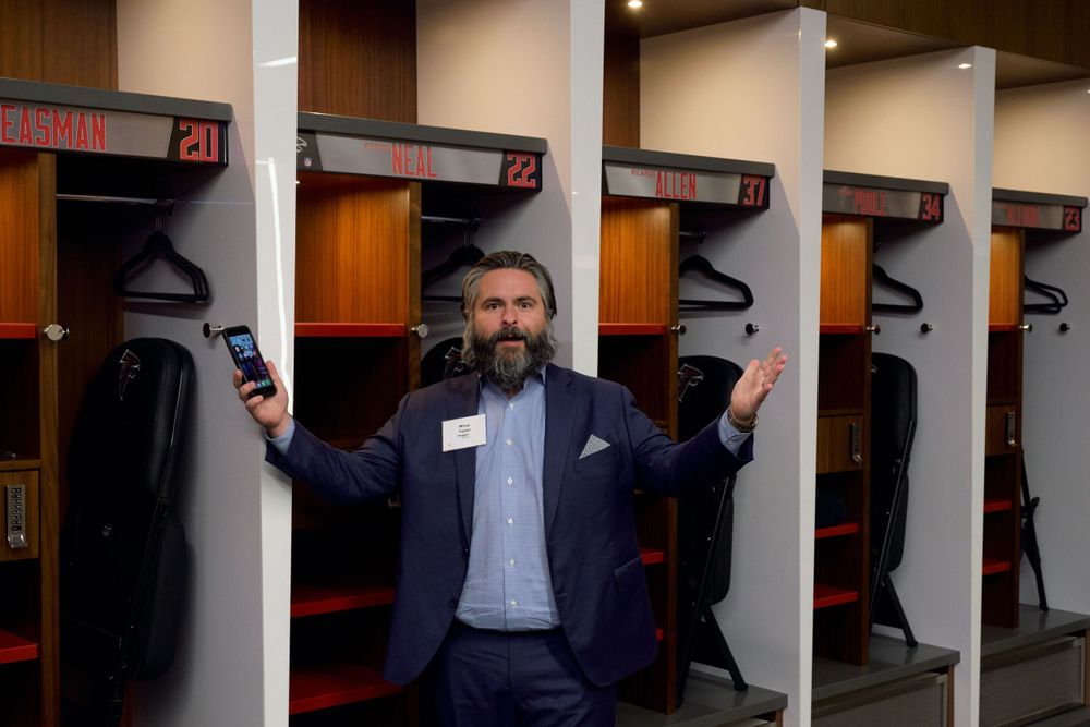 Man in suit poses in front of stadium lockers.